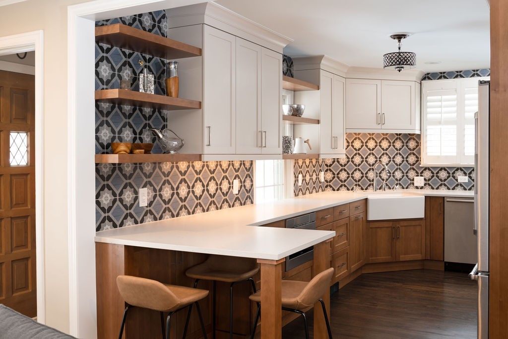 White upper cabinets, maple lower cabinets, white quartz countertops, kitchen island bar seating and patterned tile backsplash make up this remodeled mid-century modern farmhouse kitchen.